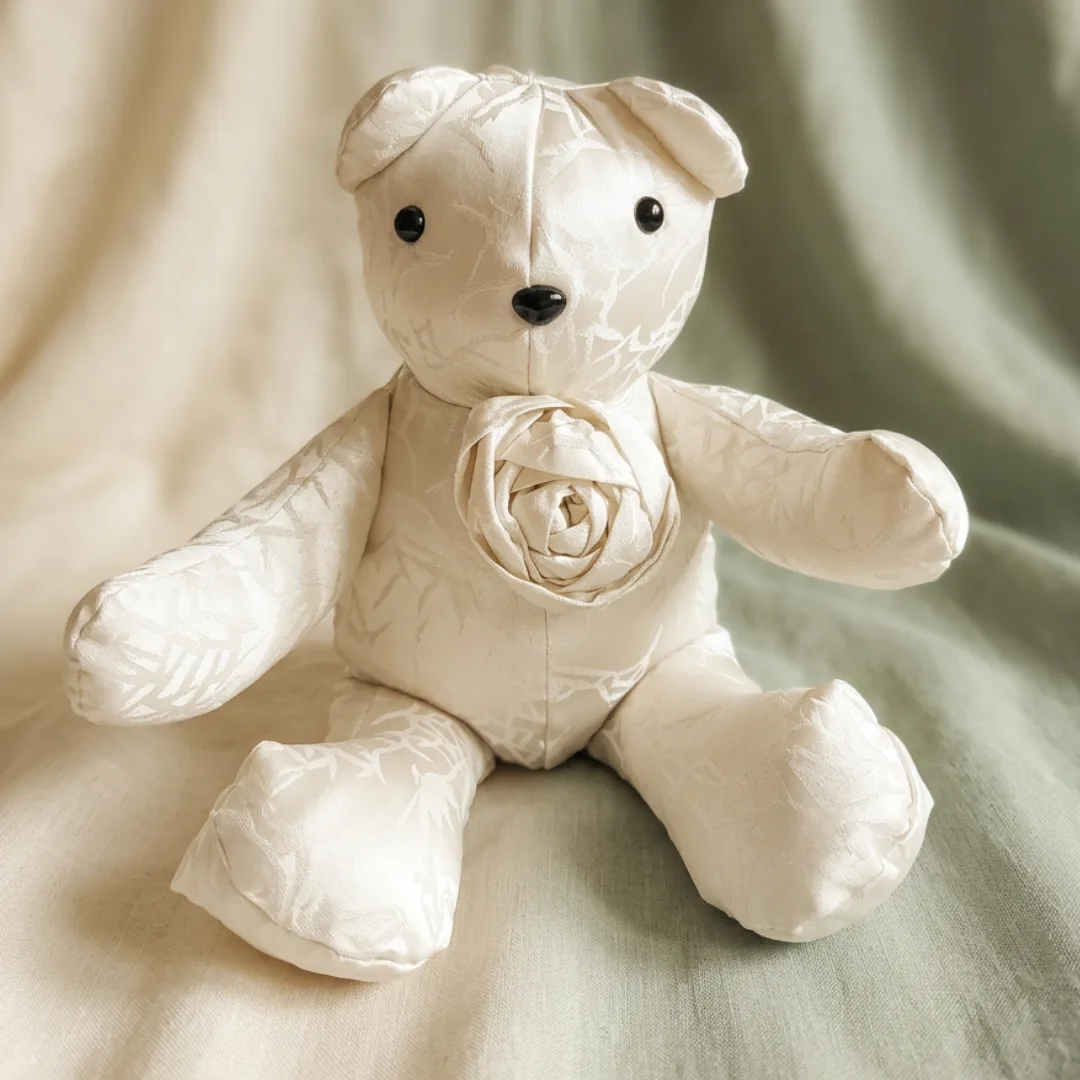 Ivory wedding dress memory bear with a hand rolled fabric rose on its chest, sitting on soft fabric